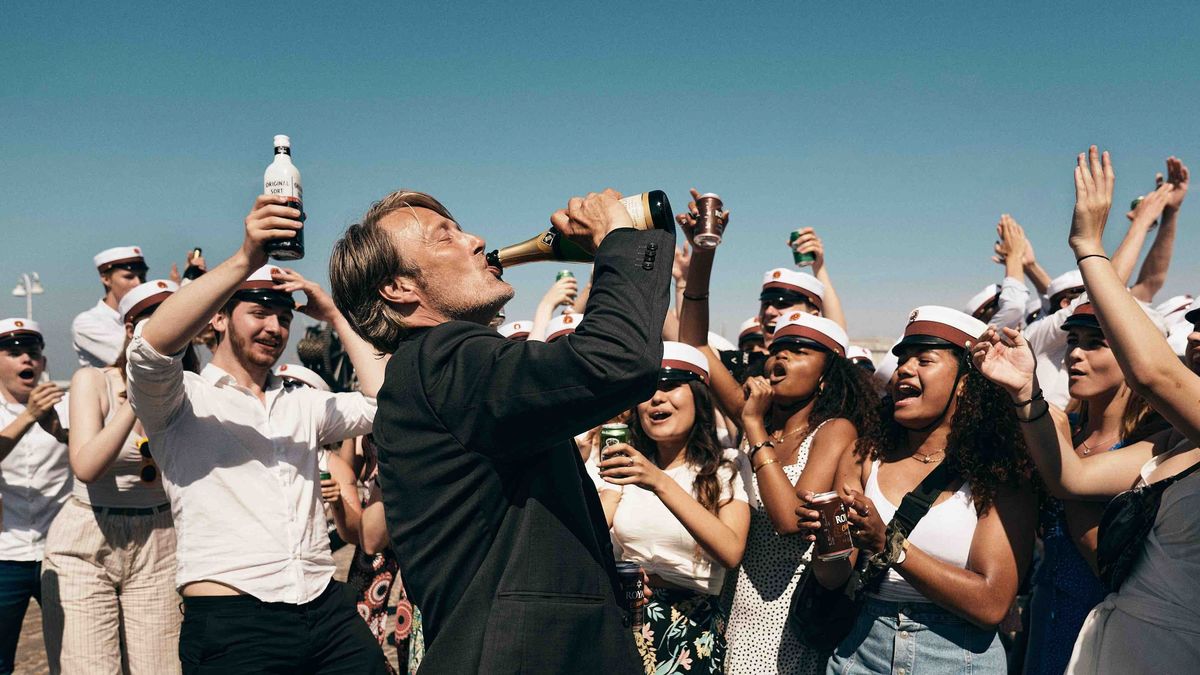 Mads Mikkelsen bebe de una botella de champán, rodeado de jóvenes con trajes de marinero, en Another Round - best hulu movies